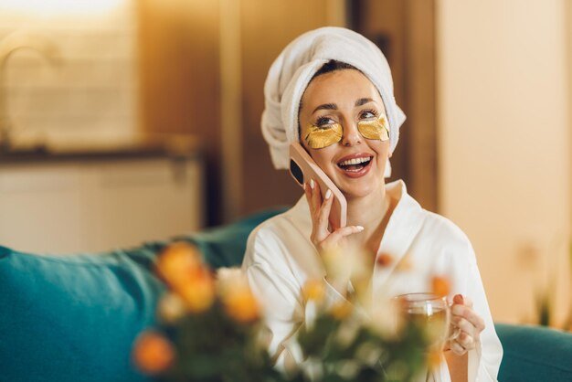 attractive woman with skincare eye patches using smartphone while enjoying morning coffee her home_360066 25581